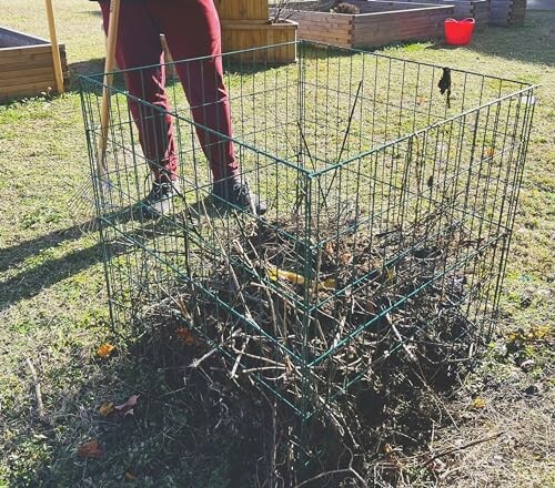 Person standing by a wire compost bin filled with sticks and leaves.