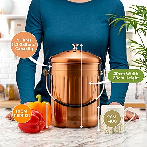 Copper compost bin on kitchen counter with pepper and mug for size comparison.