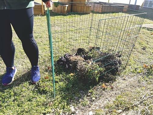 Person standing next to a garden fence with soil